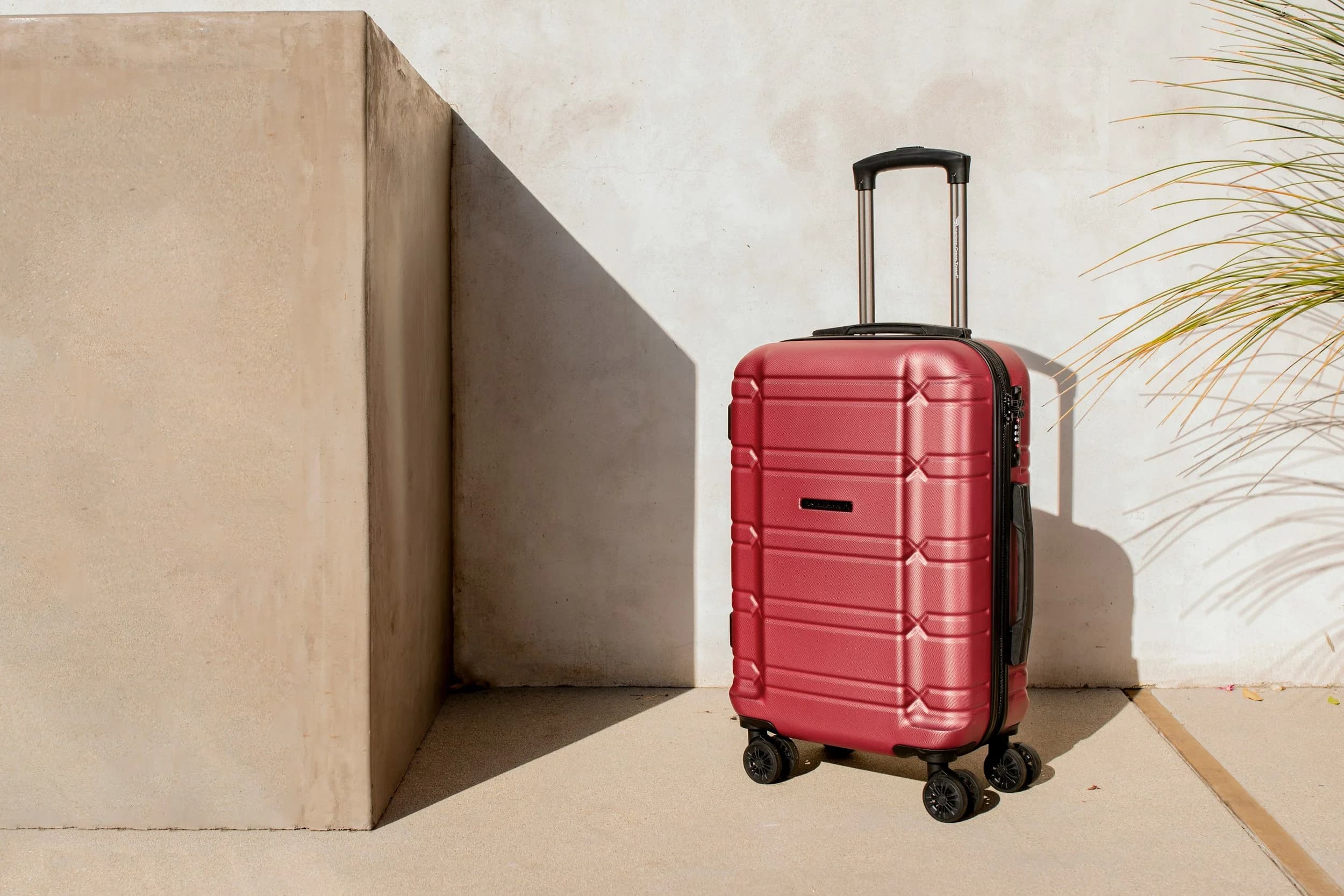 A red suitcase against a sunlit wall